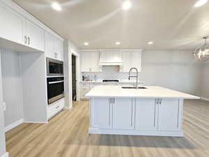 Kitchen with a kitchen island with sink, sink, white cabinets, and oven