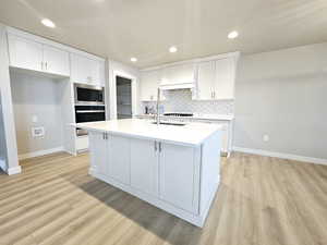 Kitchen featuring white cabinetry, premium range hood, wall oven, a kitchen island with sink, and stainless steel microwave