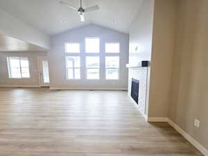 Unfurnished living room with light wood-type flooring, ceiling fan, lofted ceiling, and a tiled fireplace