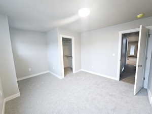 Unfurnished bedroom with light colored carpet, a closet, and a walk in closet