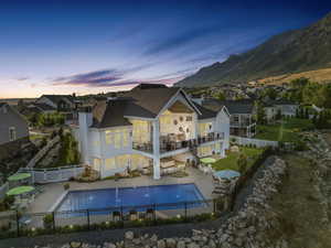 Back house at dusk featuring a patio area, pool water feature, a mountain view, a balcony, and a fenced in pool