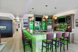 Bar with decorative light fixtures, stone counters, light hardwood / wood-style flooring, a textured ceiling, and stainless steel fridge