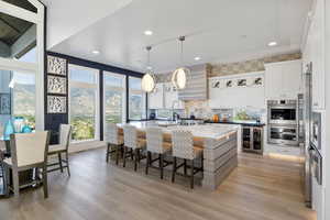 Kitchen featuring light wood-type flooring, beverage cooler, white cabinetry, and a center island with sink