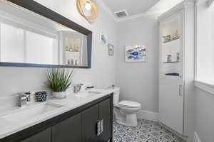 Bathroom with toilet, vanity, tile patterned floors, and crown molding