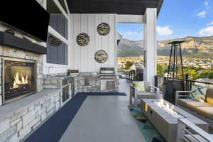 View of patio / terrace with a mountain view, an outdoor living space with a fireplace, and exterior kitchen