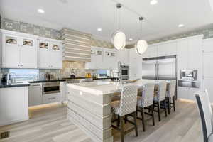 Kitchen with white cabinetry, an island with sink, stainless steel appliances, hanging light fixtures, and sink