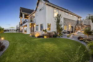 Back house at dusk featuring a lawn and a patio area