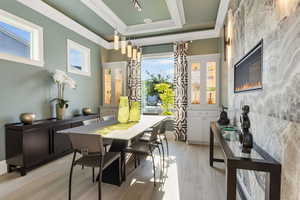 Dining space with a raised ceiling, a healthy amount of sunlight, ornamental molding, and light hardwood / wood-style floors