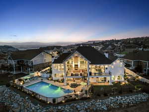 Back house at dusk featuring a fenced in pool, a balcony, and a patio