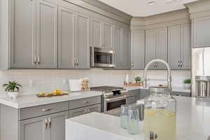 Kitchen with appliances with stainless steel finishes, tasteful backsplash, light stone counters, and gray cabinets