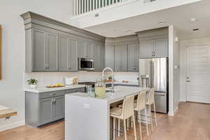 Kitchen featuring appliances with stainless steel finishes, an island with sink, gray cabinets, and light hardwood / wood-style floors