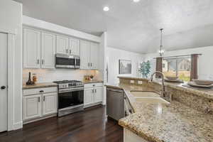 Kitchen with light stone countertops, pendant lighting, white cabinetry, appliances with stainless steel finishes, and sink. Plantation shutters