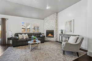 Great room featuring dark wood-type flooring, a stone fireplace, and vaulted ceiling. plantation shutters.