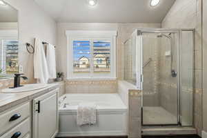 Bathroom featuring separate shower and tub, vaulted ceiling, and vanity