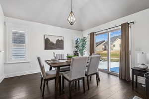 Dining space with a healthy amount of sunlight, a chandelier, lofted ceiling, and dark hardwood / wood-style floors. plantation shutters.