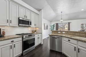 Kitchen featuring light stone counters, pendant lighting, stainless steel appliances, lofted ceiling, and white cabinets