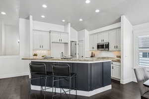 Kitchen with light stone countertops, vaulted ceiling, a center island with sink, a breakfast bar, and tasteful backsplash