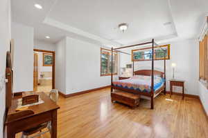 Bedroom with light hardwood / wood-style floors, a raised ceiling, and ensuite bath