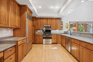 Kitchen with appliances with stainless steel finishes, sink, light stone counters, and light hardwood / wood-style floors