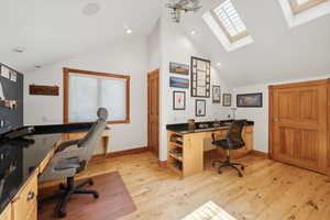 Home office featuring built in desk, light wood-type flooring, and lofted ceiling with skylight