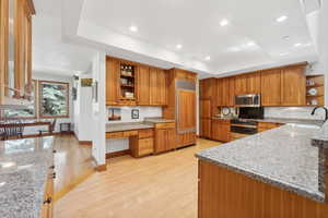 Kitchen with sink, a tray ceiling, light wood-type flooring, stainless steel appliances, and light stone counters