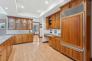 Kitchen with light stone counters, light hardwood / wood-style floors, paneled fridge, and a raised ceiling