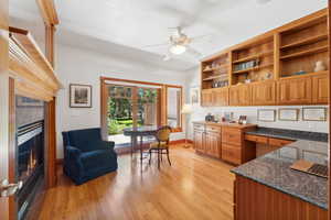 Kitchen featuring ceiling fan, dark stone counters, built in desk, and light hardwood / wood-style floors