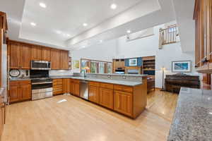 Kitchen with light stone countertops, appliances with stainless steel finishes, kitchen peninsula, and light wood-type flooring