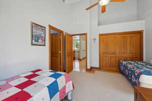 Bedroom with ceiling fan, light colored carpet, and a high ceiling