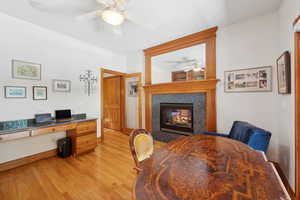 Office space with ceiling fan, light wood-type flooring, and a multi sided fireplace