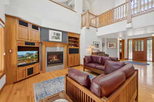 Living room with light wood-type flooring, beamed ceiling, a high ceiling, and built in shelves