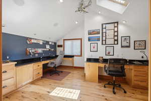 Office space with light hardwood / wood-style floors, high vaulted ceiling, a skylight, and built in desk