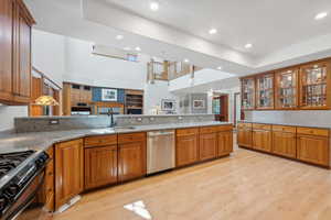 Kitchen with range with gas cooktop, dishwasher, sink, light wood-type flooring, and light stone counters