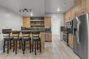 Kitchen featuring appliances with stainless steel finishes, tasteful backsplash, light hardwood / wood-style floors, sink, and a breakfast bar