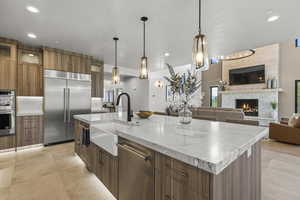 Kitchen with decorative light fixtures, a fireplace, sink, appliances with stainless steel finishes, and an island with sink