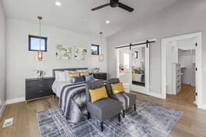 Bedroom with ceiling fan, a walk in closet, a barn door, and wood-type flooring