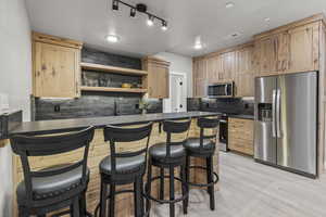 Kitchen with appliances with stainless steel finishes, light brown cabinets, tasteful backsplash, a kitchen breakfast bar, and light wood-type flooring