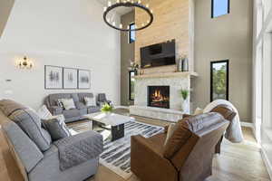 Living room with light wood-type flooring, a high ceiling, a stone fireplace, and a notable chandelier