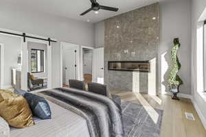 Bedroom featuring ensuite bathroom, a barn door, hardwood / wood-style flooring, ceiling fan, and a tiled fireplace