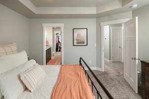 Bedroom featuring a walk in closet, connected bathroom, a closet, light colored carpet, and a tray ceiling