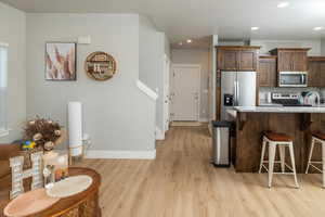 Kitchen with light hardwood / wood-style floors, a breakfast bar area, stainless steel appliances, light stone countertops, and sink