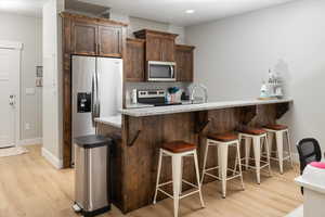 Kitchen featuring kitchen peninsula, light wood-type flooring, a kitchen breakfast bar, stainless steel appliances, and dark brown cabinets