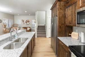 Kitchen with light stone countertops, appliances with stainless steel finishes, light hardwood / wood-style flooring, and sink