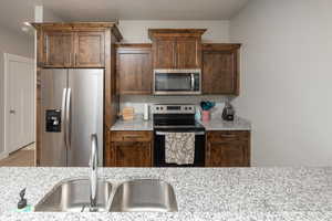 Kitchen with appliances with stainless steel finishes, light stone counters, and sink