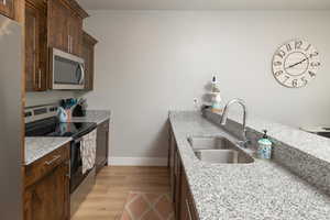 Kitchen with light stone countertops, sink, stainless steel appliances, and light hardwood / wood-style flooring