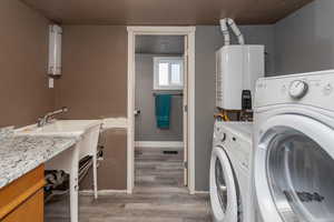 Clothes washing area featuring hardwood / wood-style flooring, washer and dryer, and tankless water heater