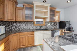 Kitchen with backsplash, light hardwood / wood-style floors, sink, stainless steel appliances, and dark stone counters