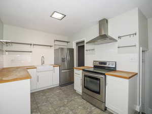 Kitchen with appliances with stainless steel finishes, butcher block counters, and range hood