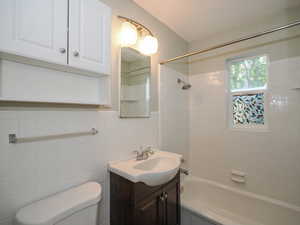 Full bathroom with tile walls, toilet, vanity, and tiled shower / bath