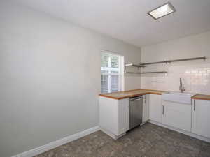 Kitchen with white cabinets, butcher block countertops, sink, and stainless steel dishwasher